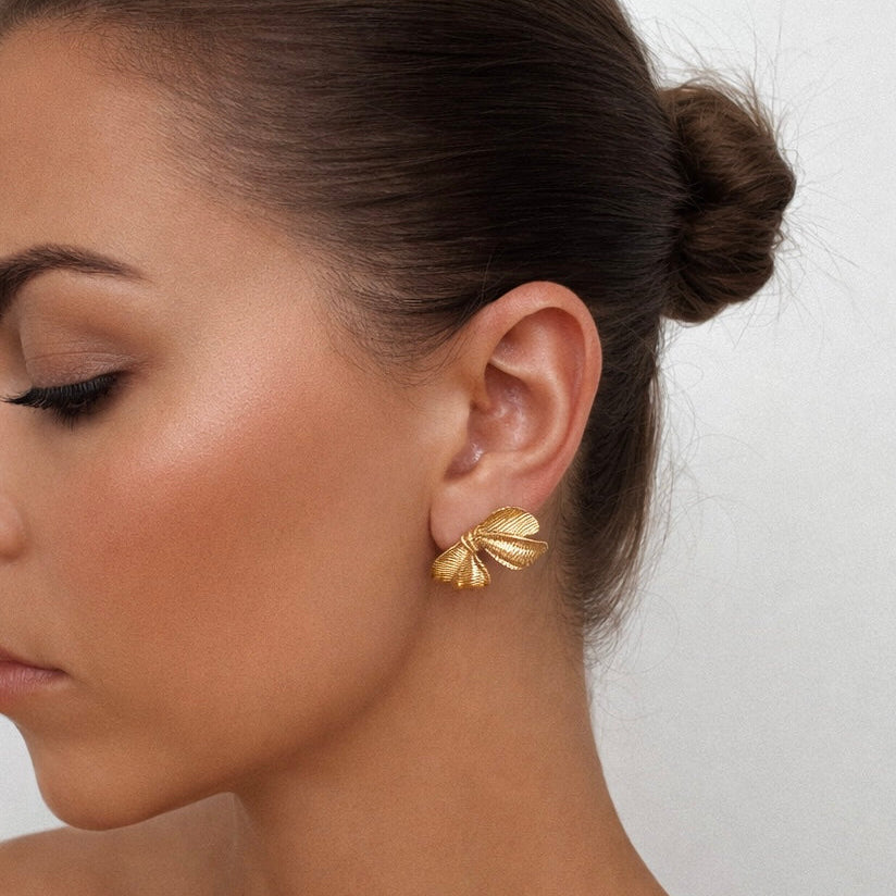 Woman wearing gold plated bow earrings.