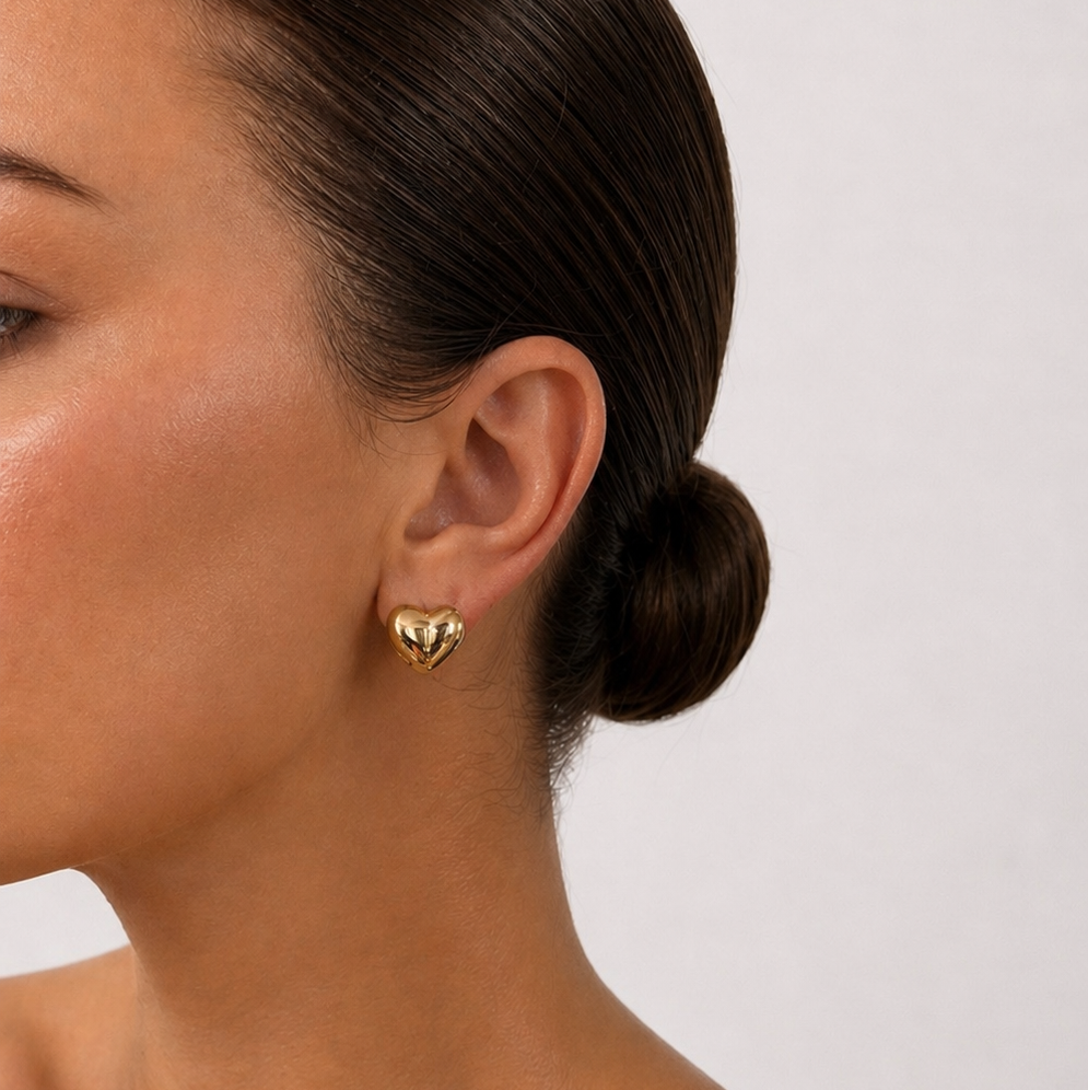 Close-up of a model wearing a gold heart-shaped earring with a plain background