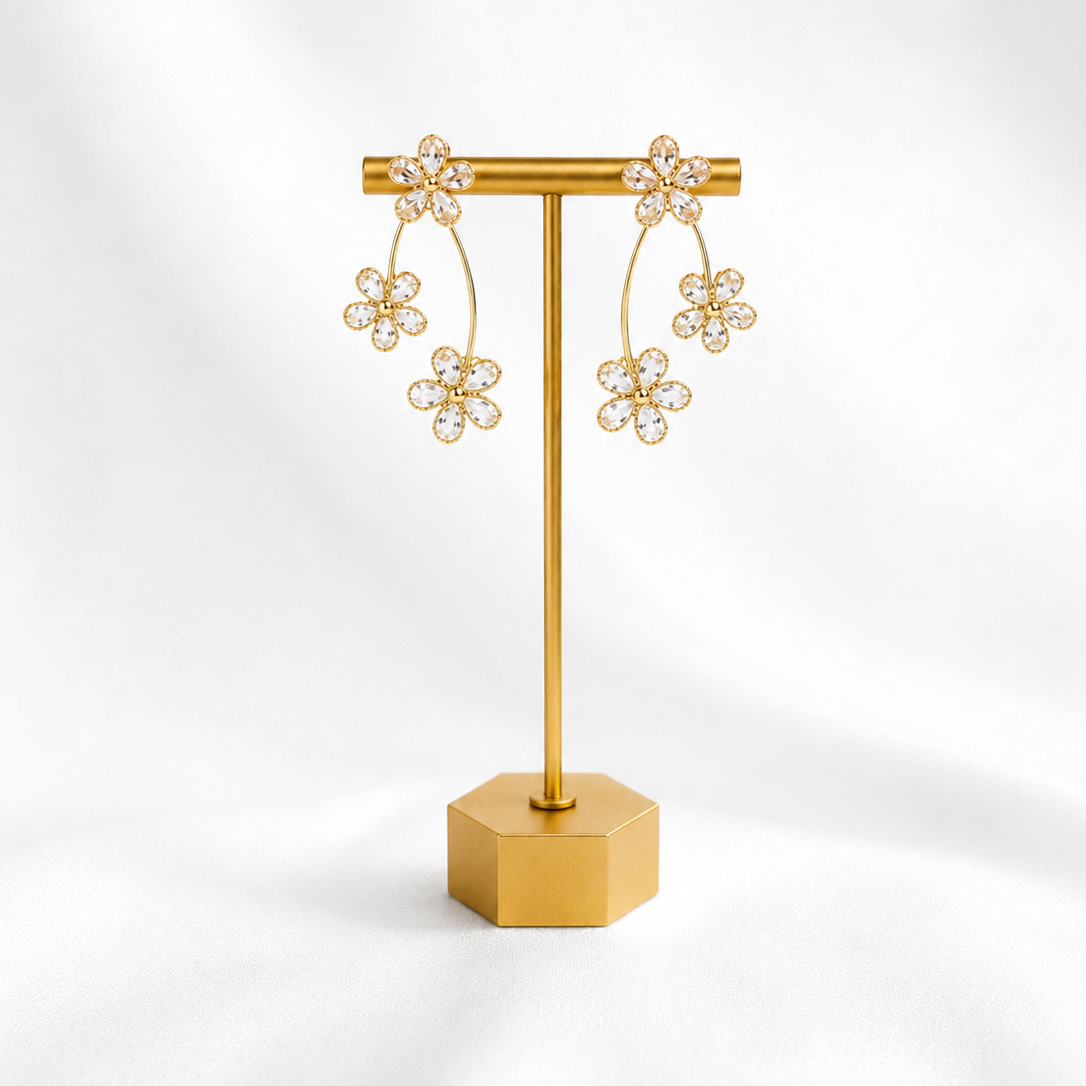 Gold earring stand with gold plated floral earrings on a white background