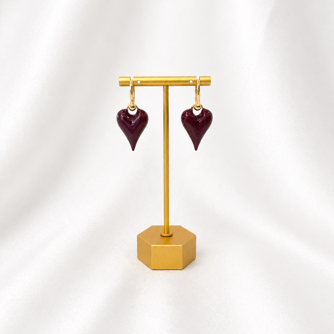 Deep cherry red heart-shaped earrings on a gold stand against a white background
