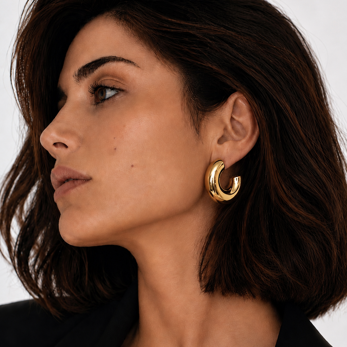 Close-up of a woman wearing gold plated hoop Lady Lou Collections earrings with a neutral background