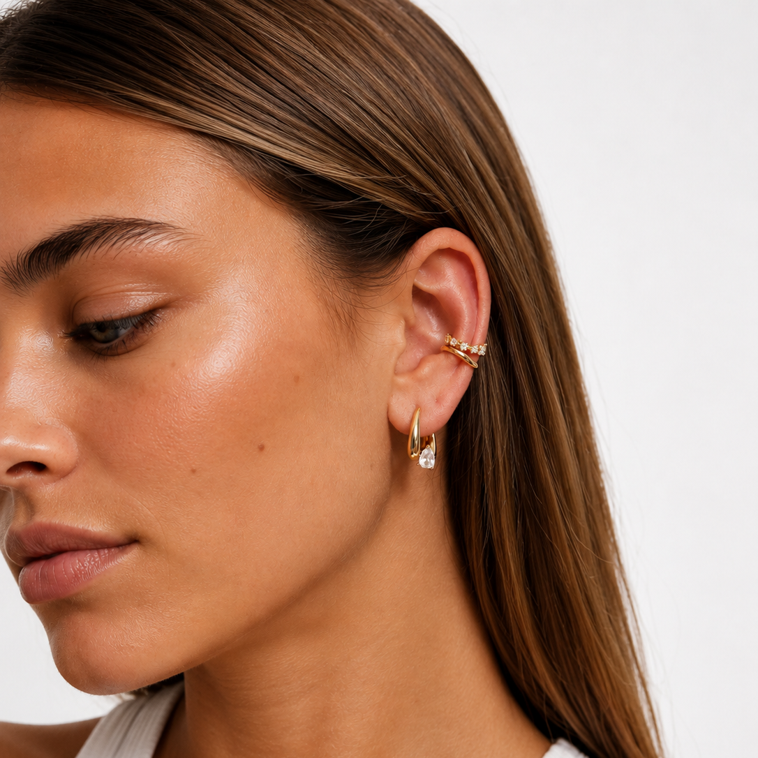 Close-up of a woman wearing gold earrings & earring cuff with a plain background