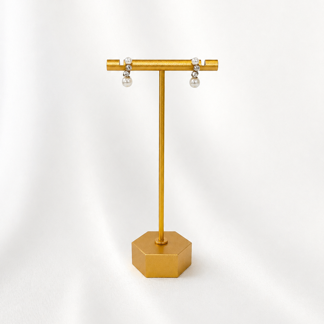 Gold jewelry stand with two pearl earrings on a white background