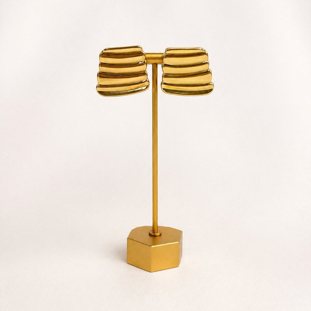 Gold Plated earring stand with two gold earrings on a light beige background
