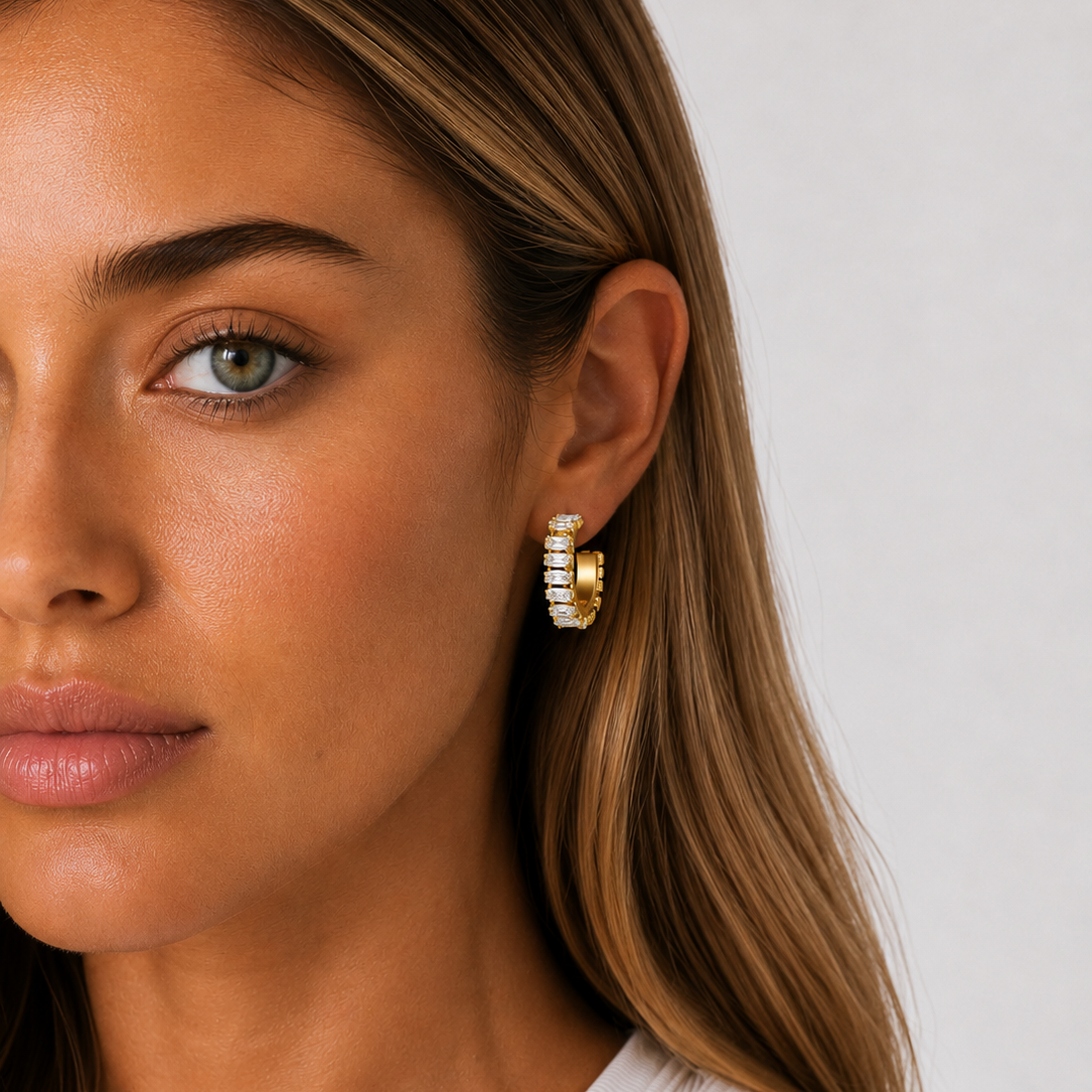 Close-up of a woman wearing gold hoop earrings with a plain background