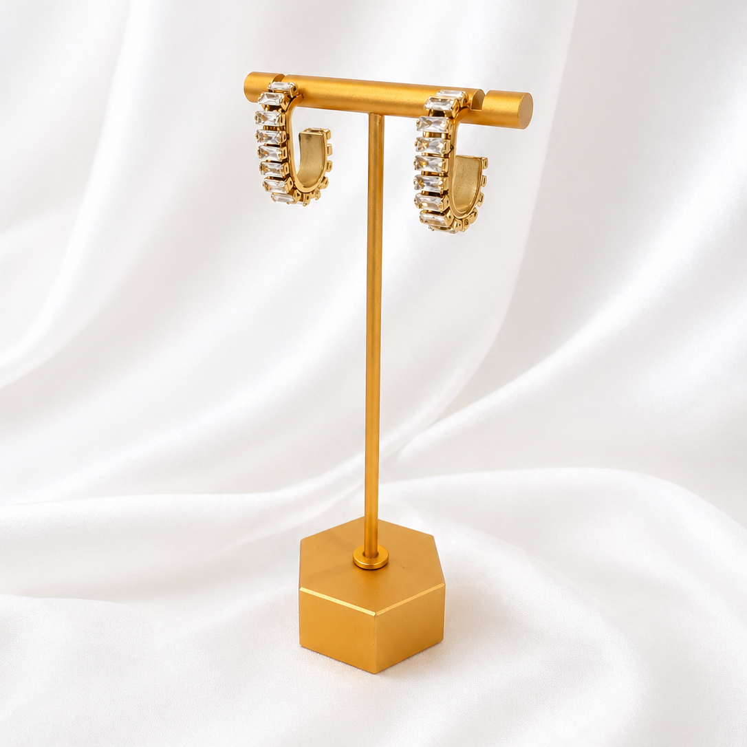 Gold earring stand with a pair of gold plated earrings on a white fabric background