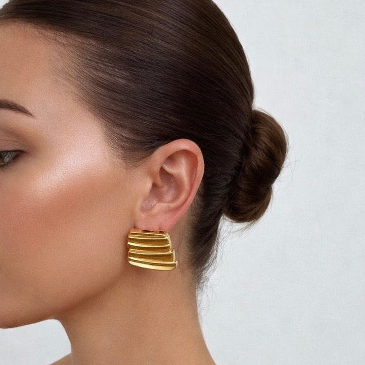 Gold plated earrings worn by a model with a plain background