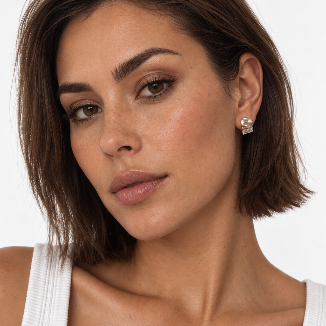A close-up of a woman  wearing a gold plated CZ stud earring, against a plain white background.
