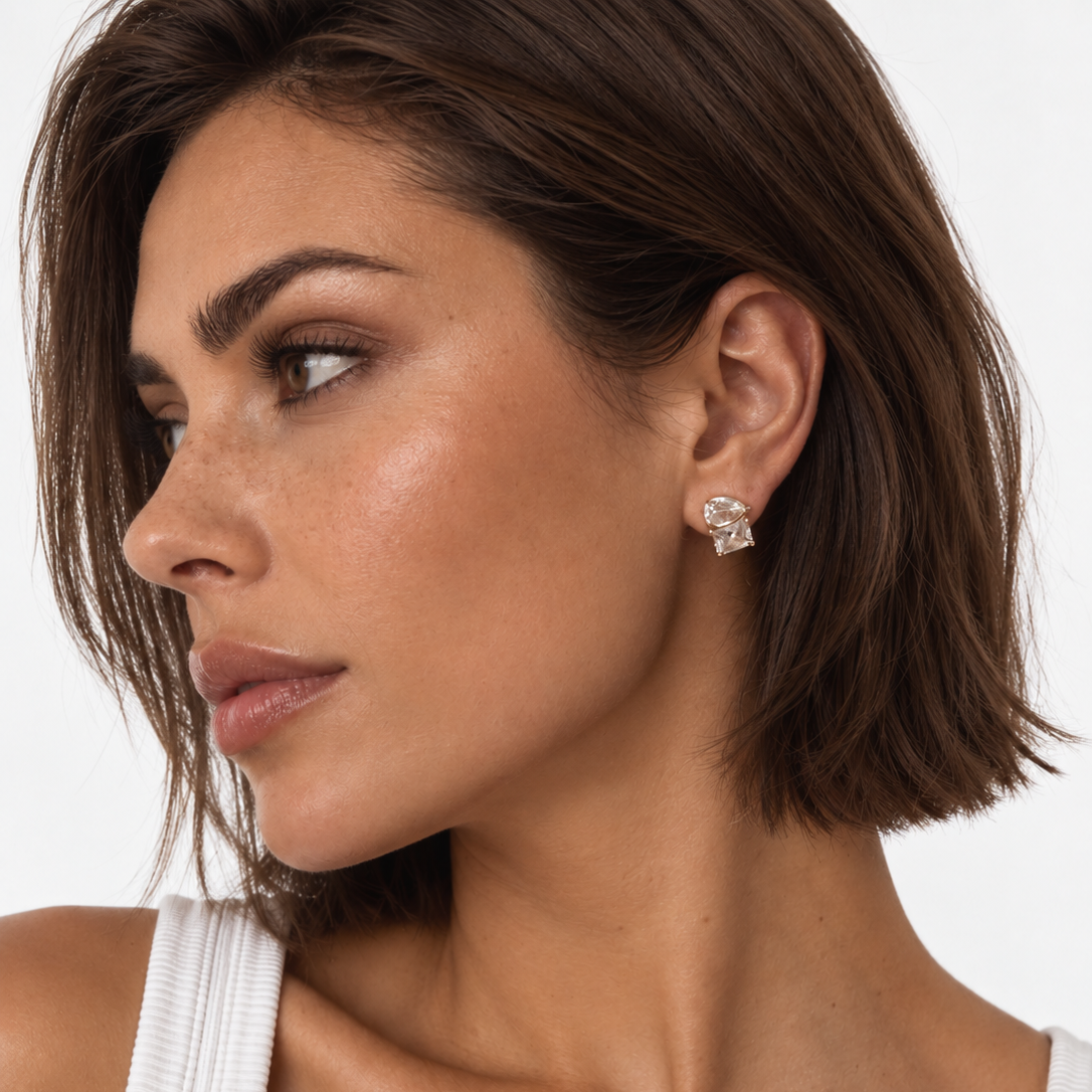 A close-up of a woman  wearing a gold plated CZ stud earring, against a plain white background.