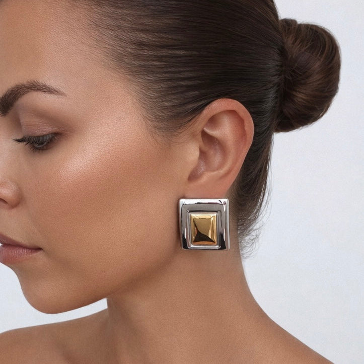 Woman wearing a square earring with a gold pyramid design on a plain background