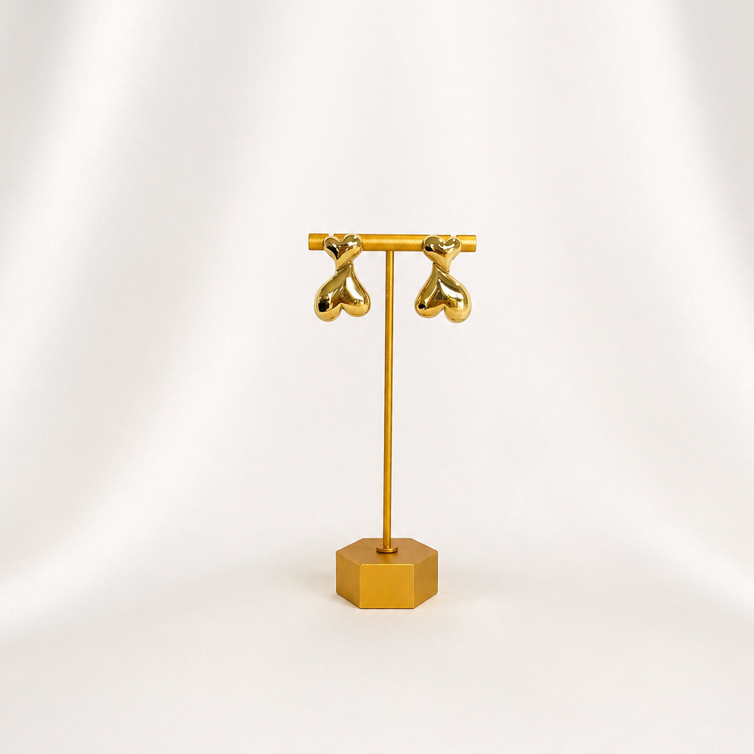 Gold plated heart earring stand with two gold earrings on a white background