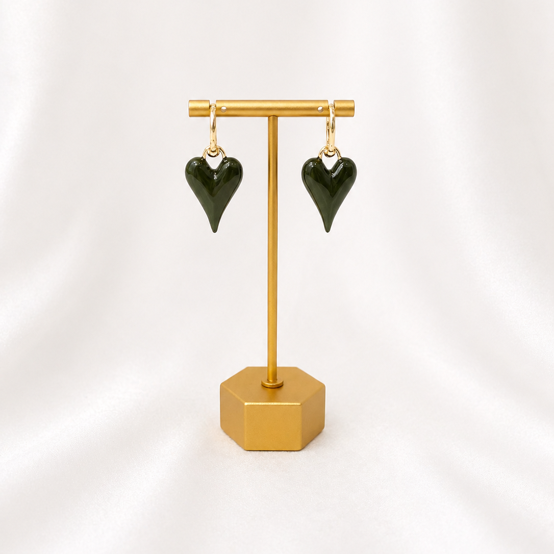 Green heart-shaped earrings on a gold plated earring stand against a white background