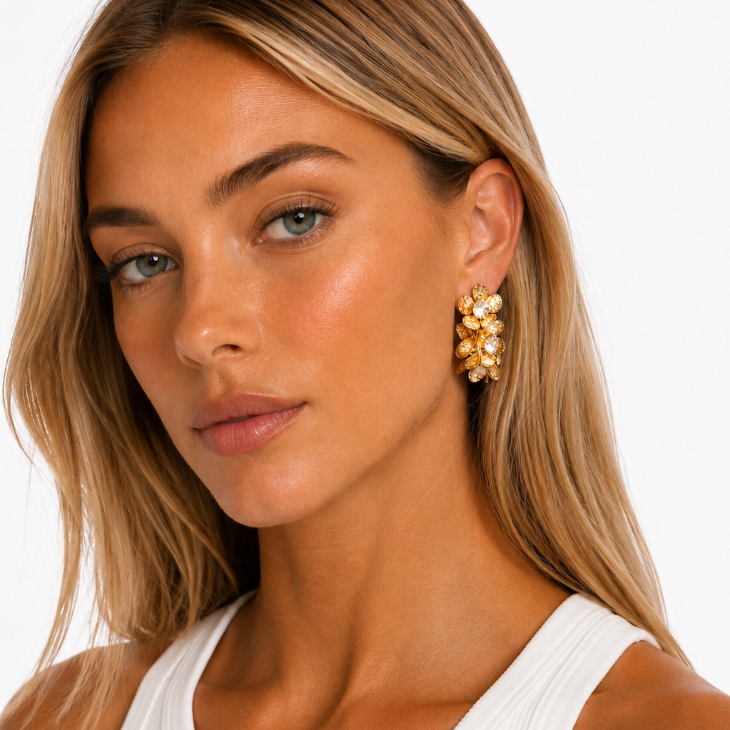 A close-up of a blonde woman wearing a white ribbed tank top and a gold floral cluster earring against a clean white background.