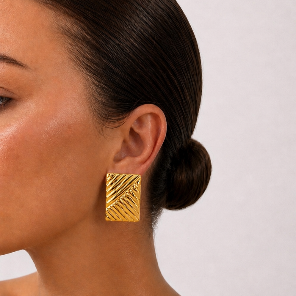 Gold plated earrings worn by a model with a plain background