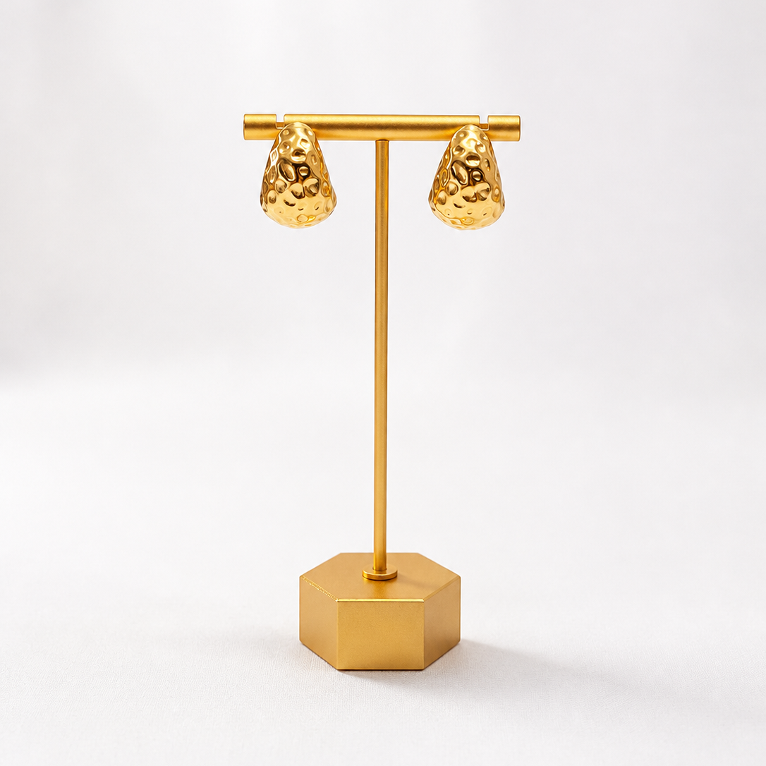 Gold plated textured earrings on gold stand and white background