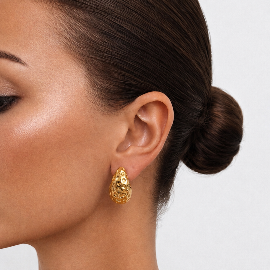 Close-up of a woman wearing gold earrings with a plain background