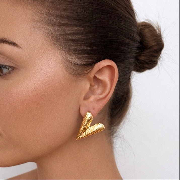 Woman wearing gold plated heart earrings with a plain background