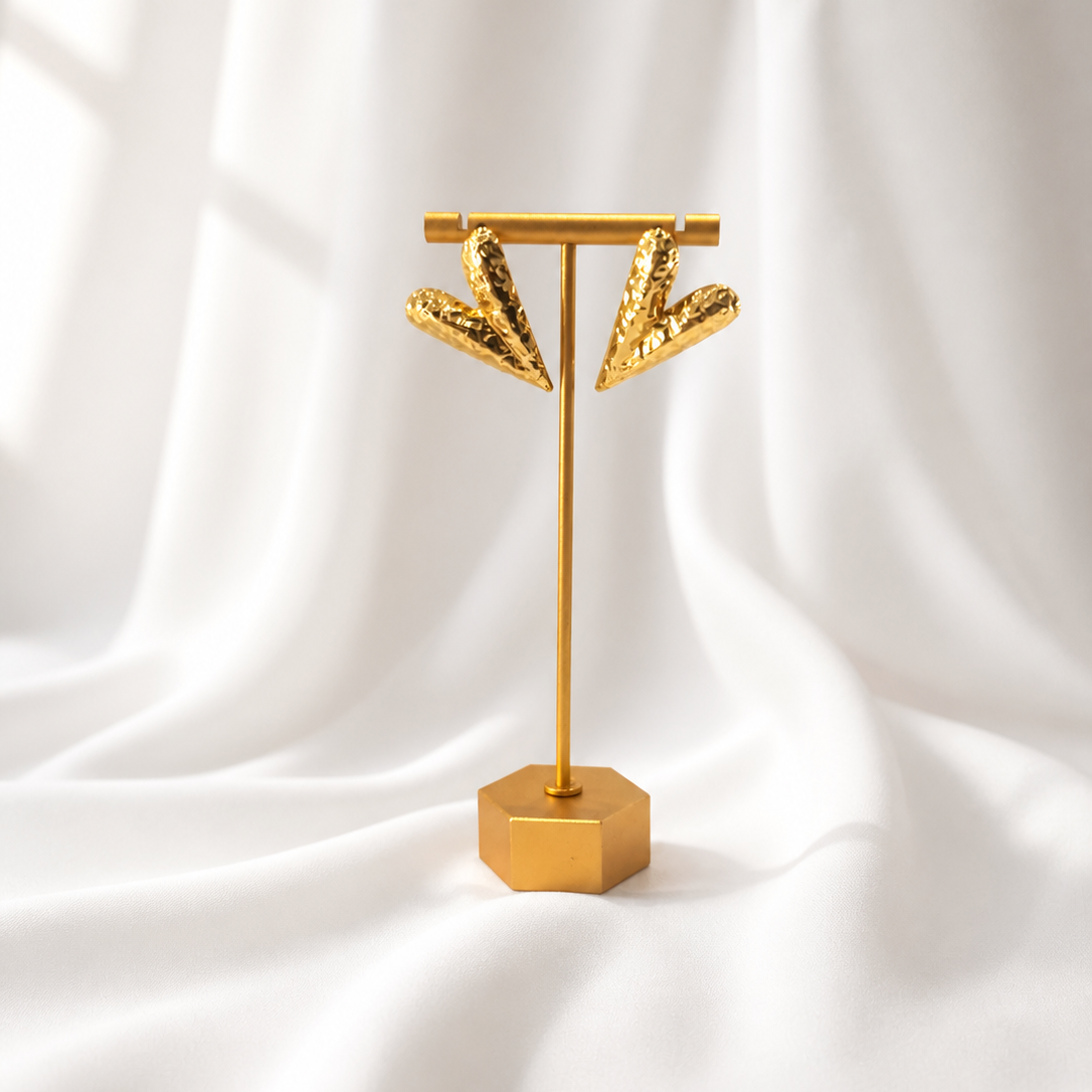 Gold earring stand with two gold earrings on a white fabric background